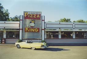 A yellow car is parked in front of a pizza king restaurant