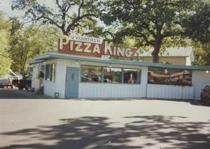 A white building with a red sign that says pizza king