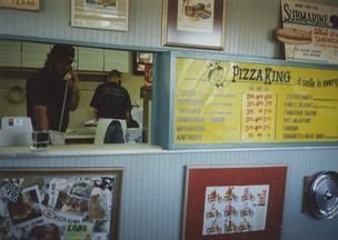A man talking on a phone in front of a pizza king menu