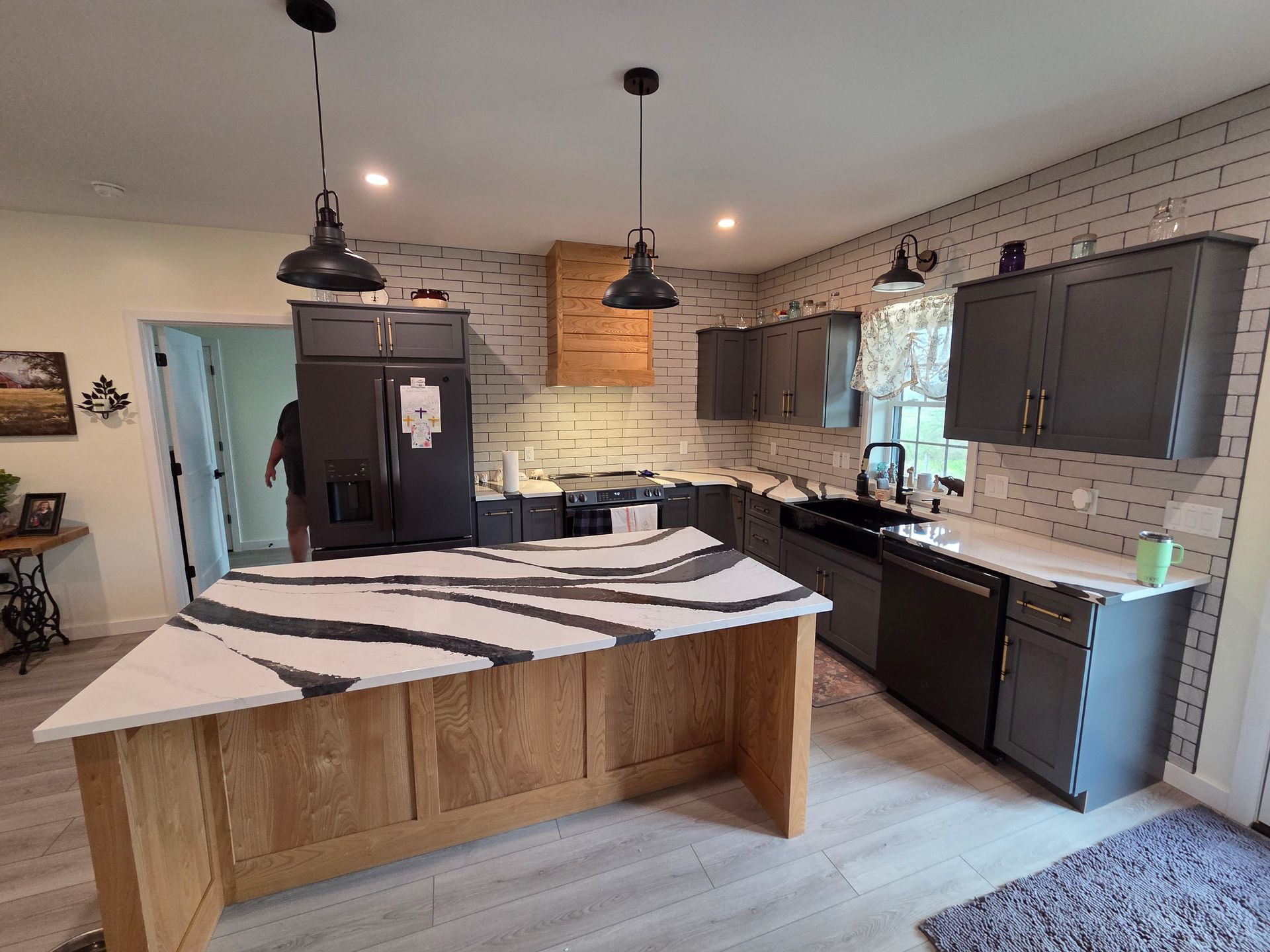 Modern kitchen with wood island, dark cabinets, white brick backsplash, and pendant lights