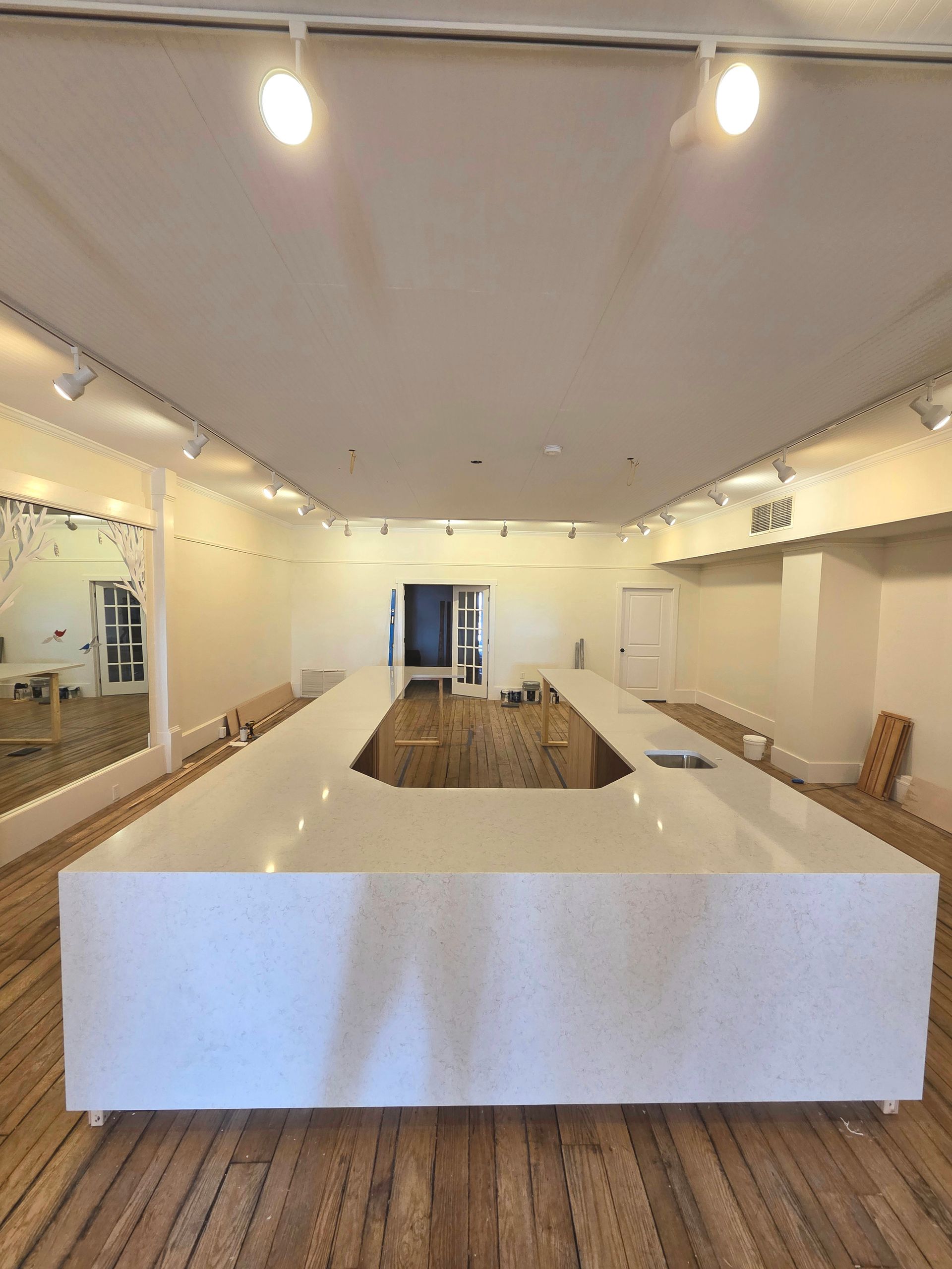 Bright, empty modern room with a long white table, mirrors on the walls, and wood flooring