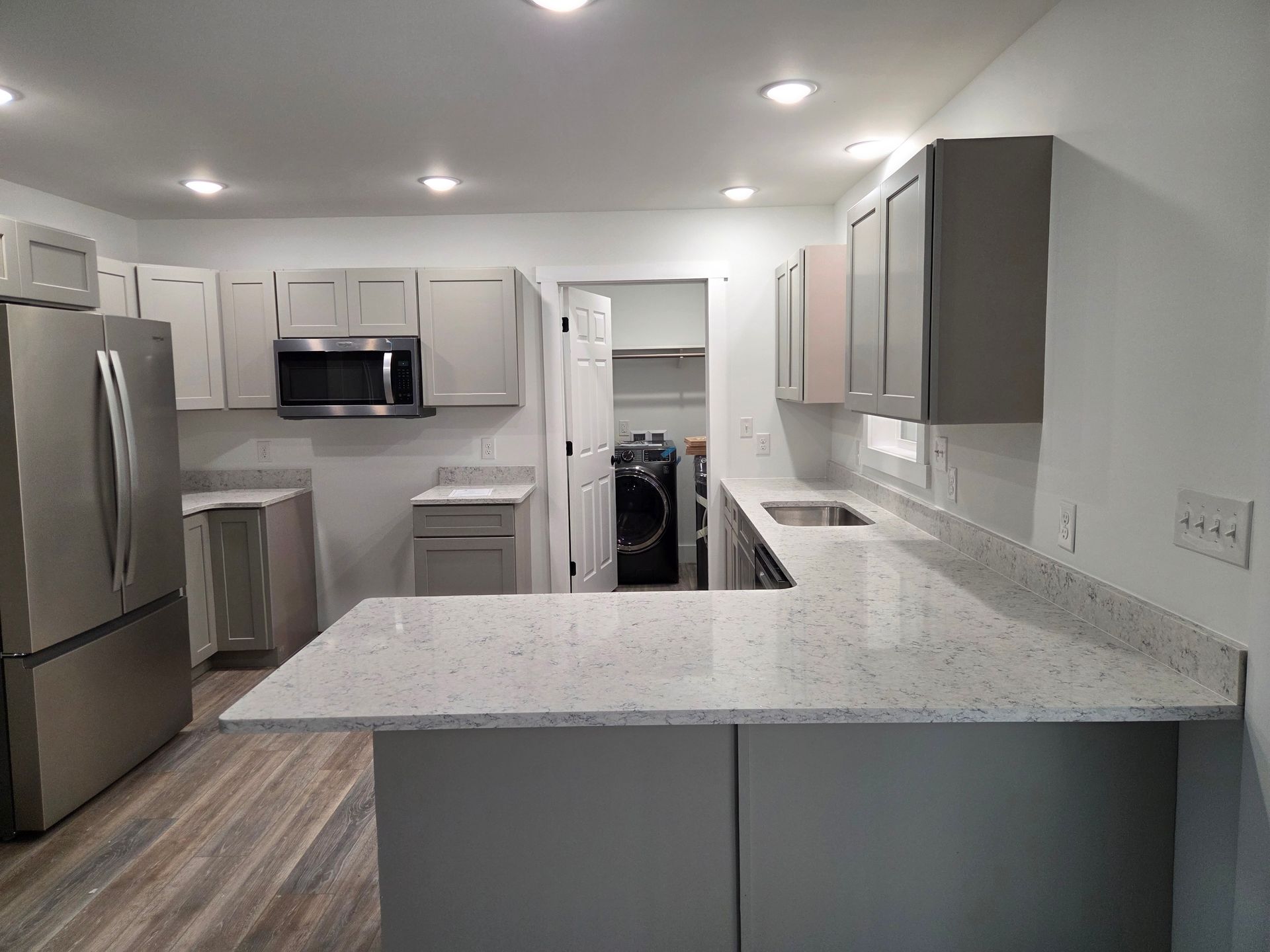 Modern white kitchen with gray cabinets, stainless appliances, and a large speckled island countertop