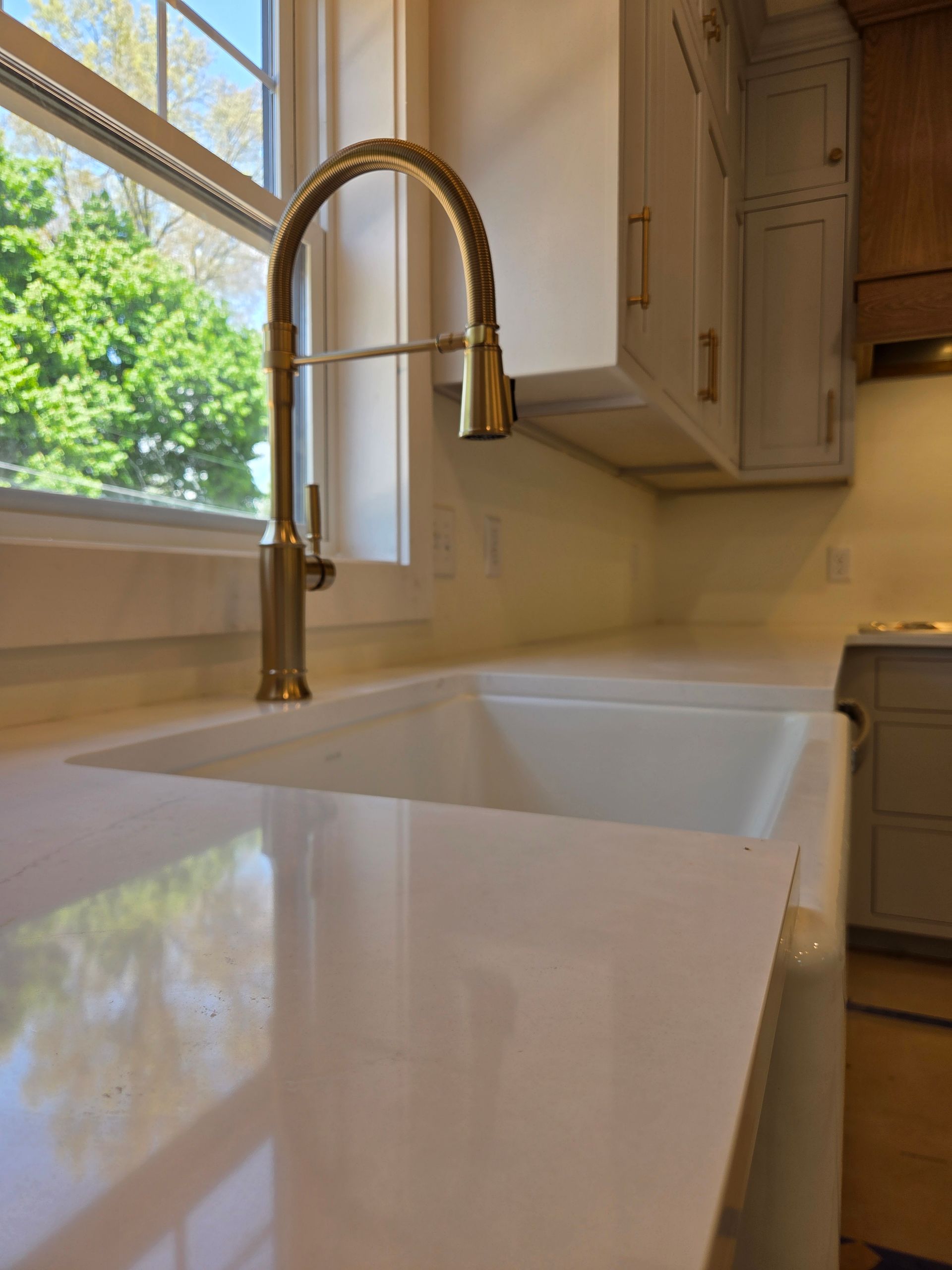 Bright kitchen sink with gold faucet beside a sunny window and white countertops