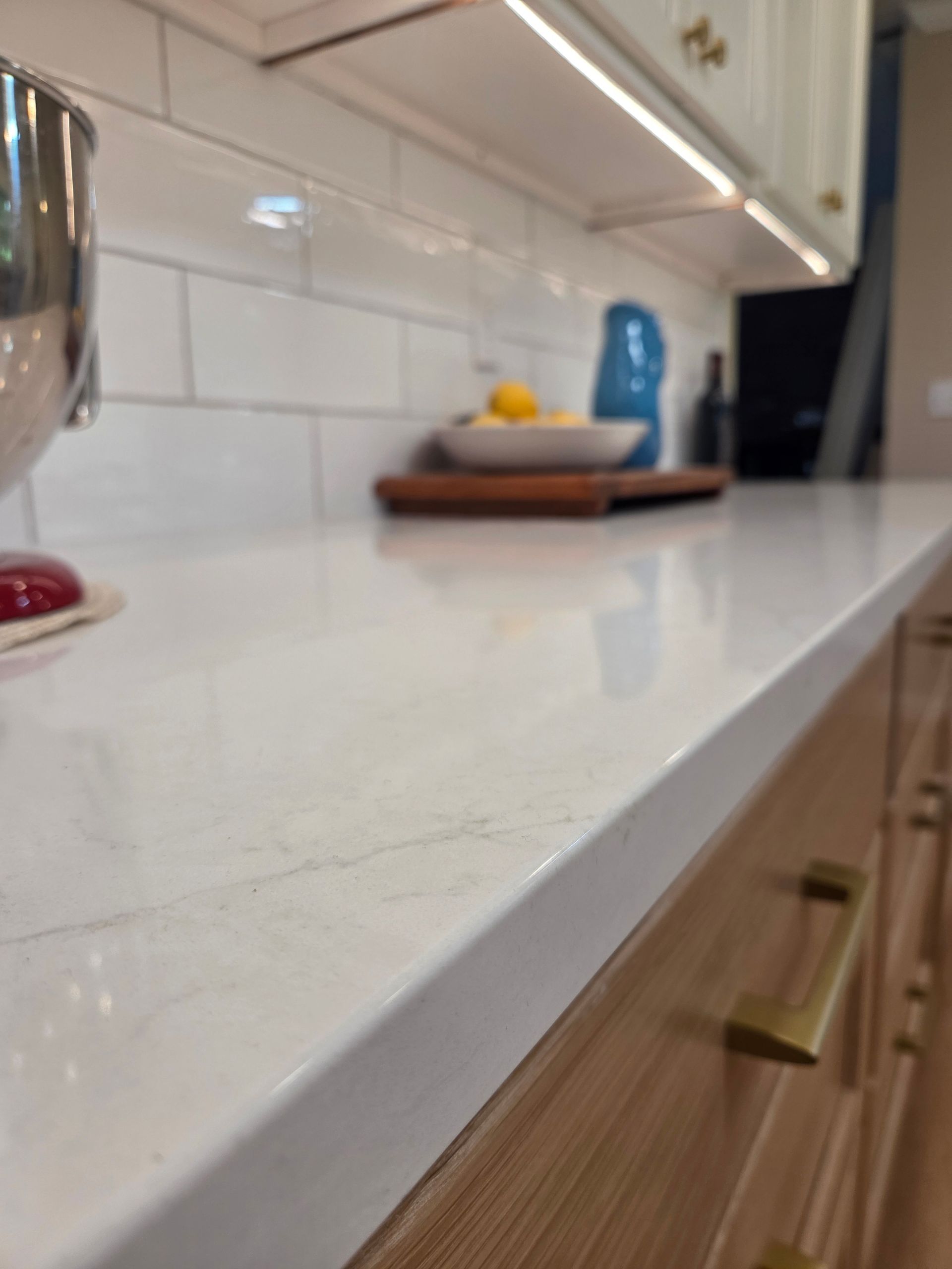 Modern kitchen countertop with white tile backsplash, wooden cabinets, and a cutting board with lemons and a blue vase