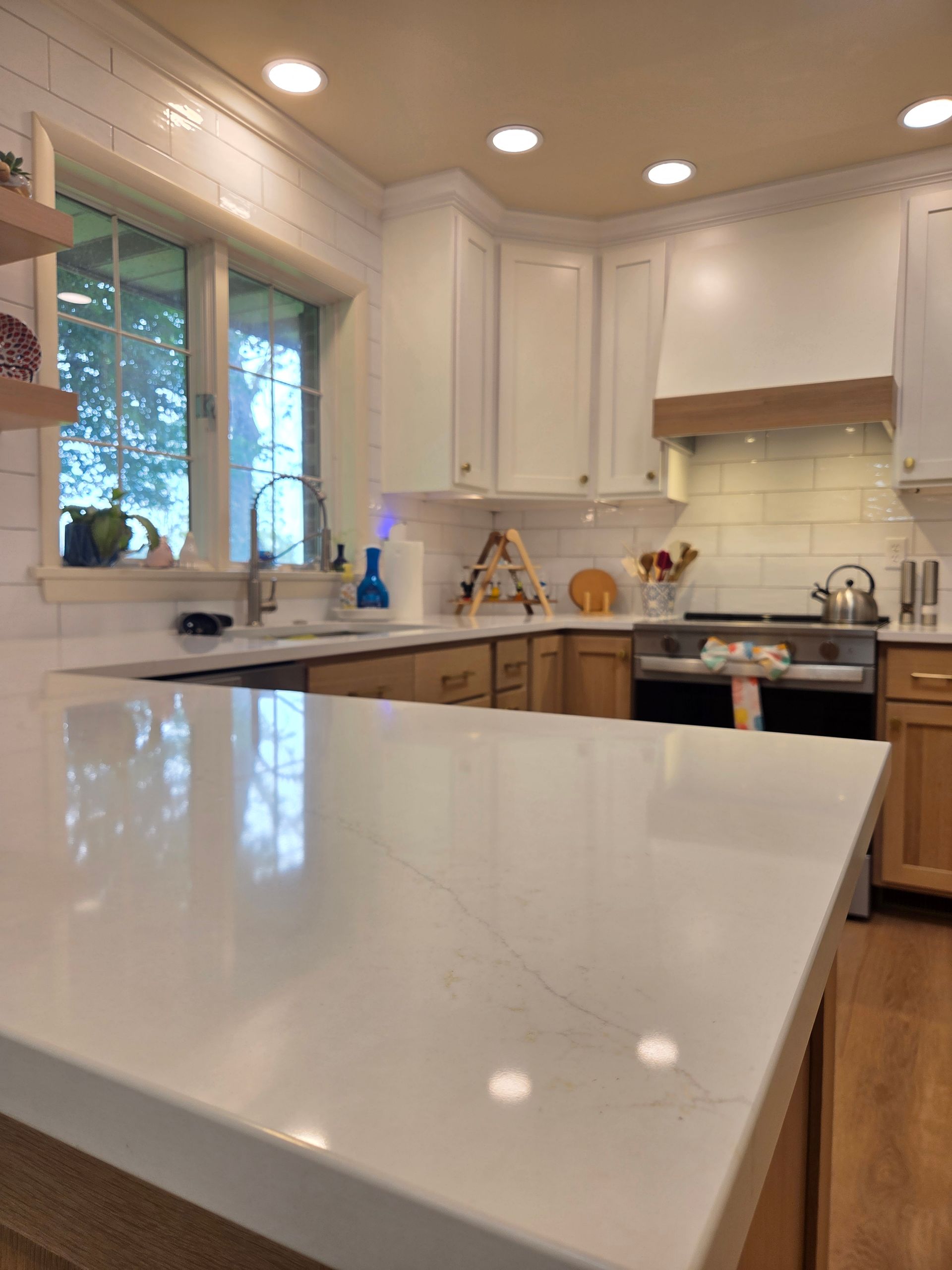 Bright modern kitchen with white cabinets, marble island, wood accents, and a window over the sink.