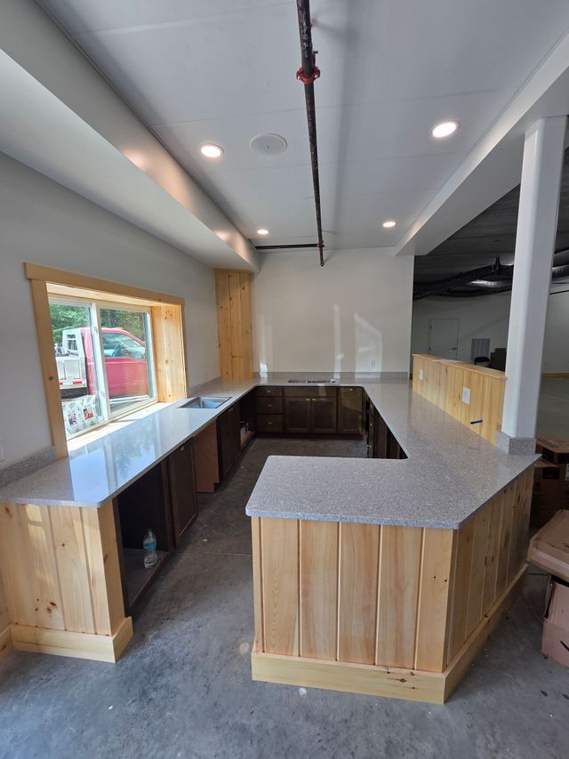 Modern kitchen with granite island, stainless sink, black cabinets, and large windows.
