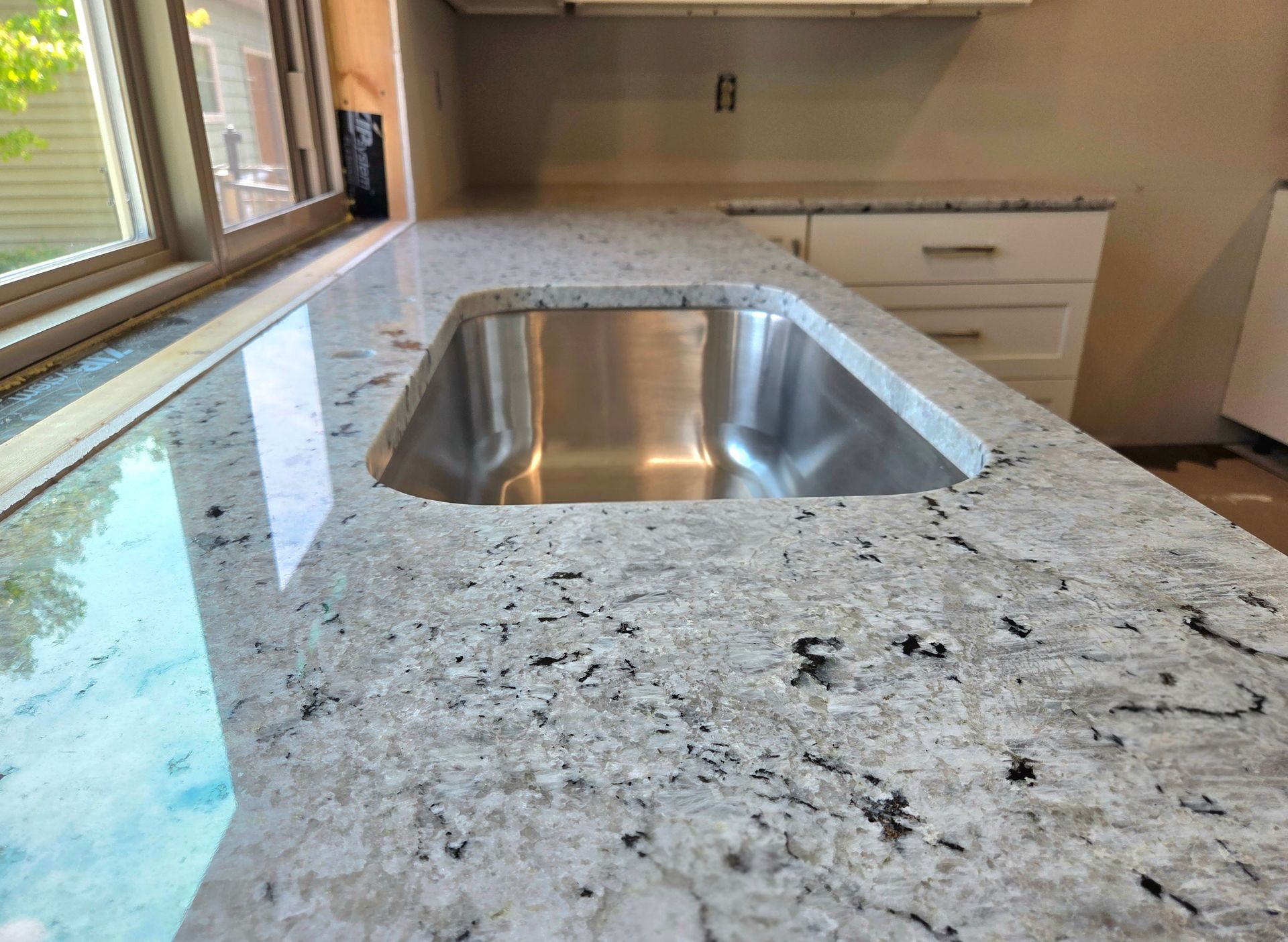 Modern kitchen countertop with a stainless steel sink and a speckled granite surface near a window