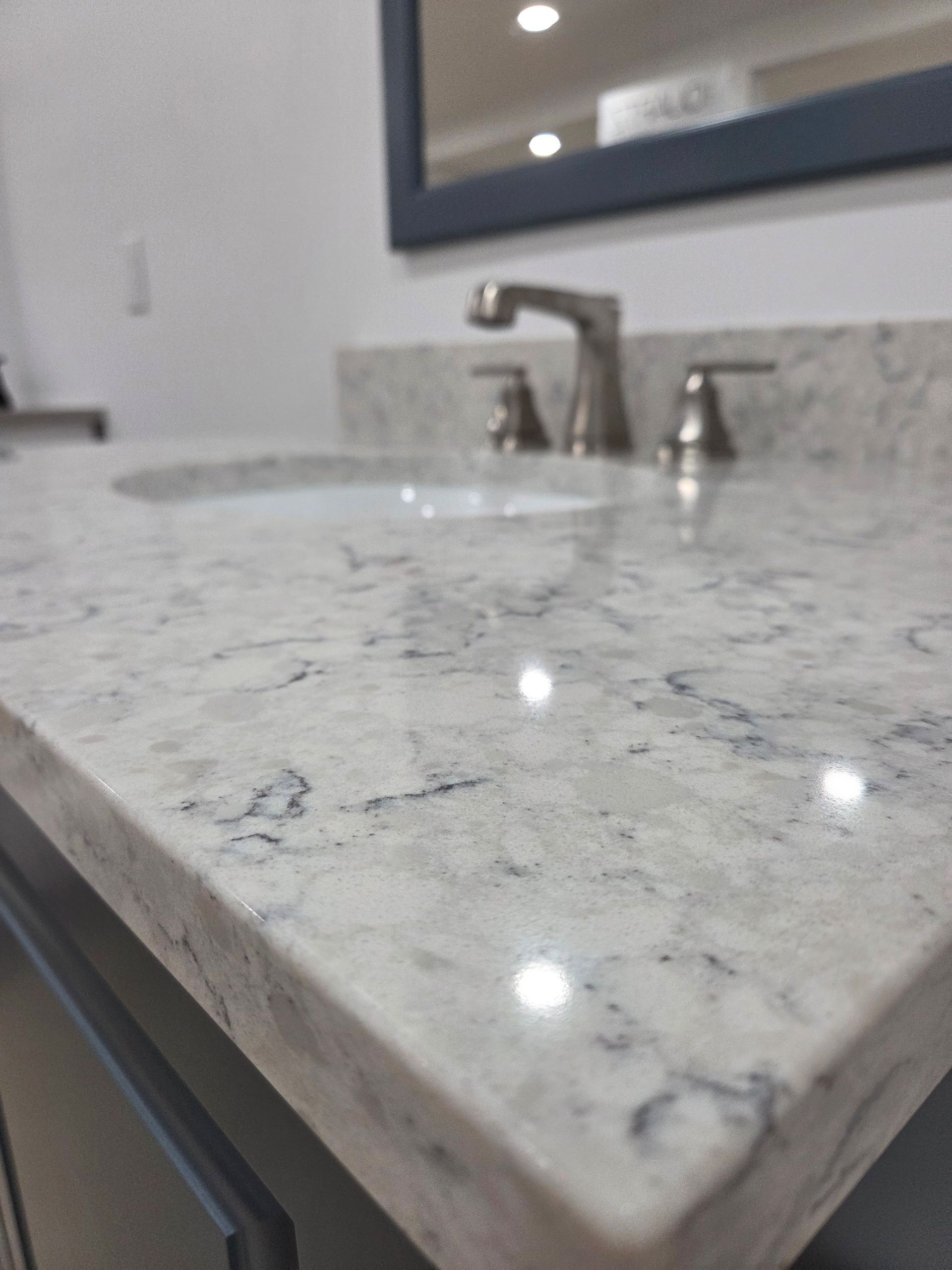 Bathroom vanity with white marble countertop, chrome faucet, and sink reflections