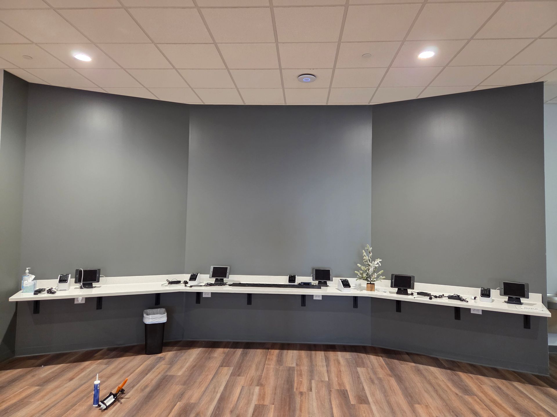 Curved conference room desk with laptops and papers against gray walls and a wood floor