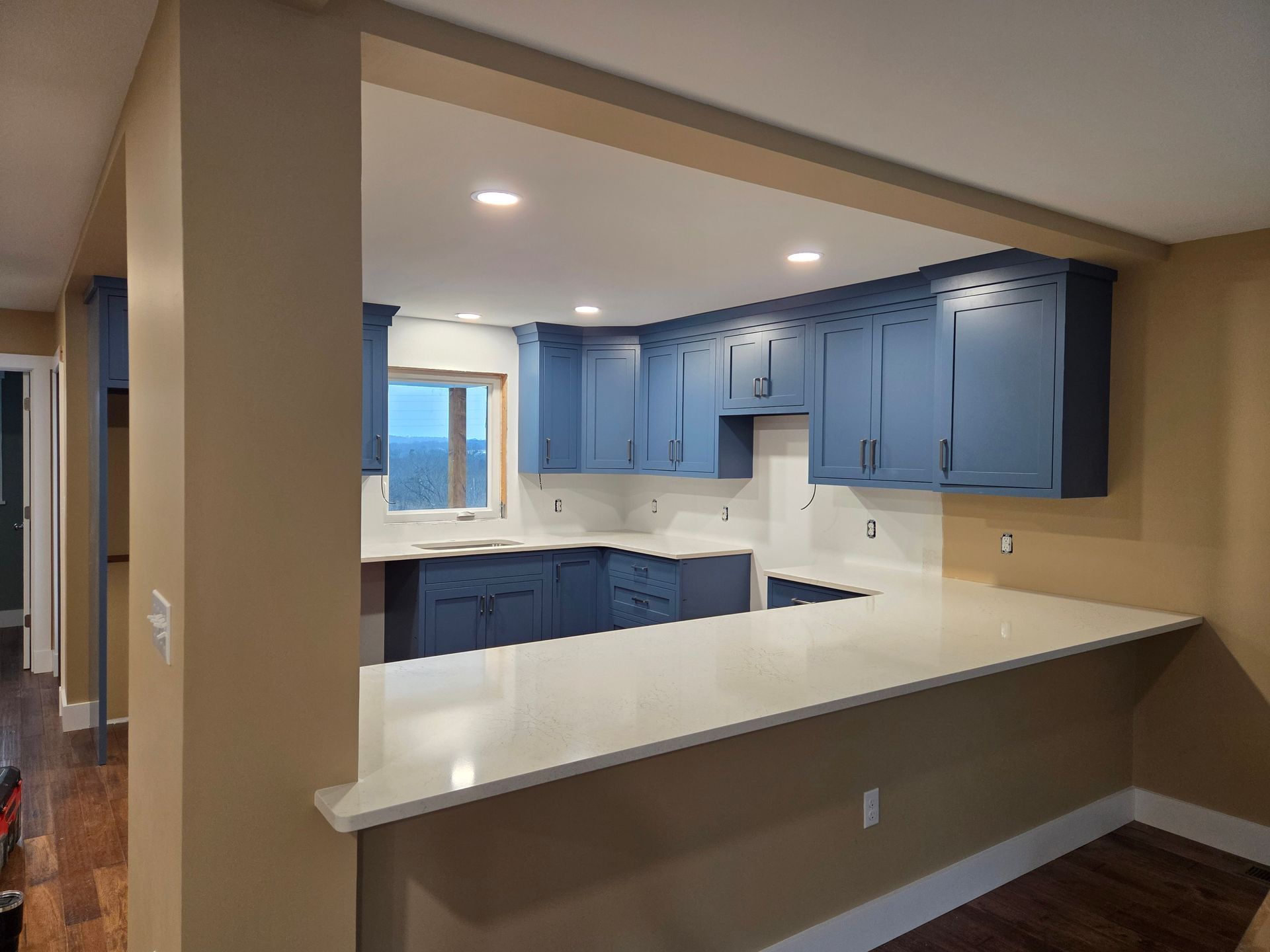 Empty kitchen with blue cabinets, white countertops, and a breakfast bar under recessed lights