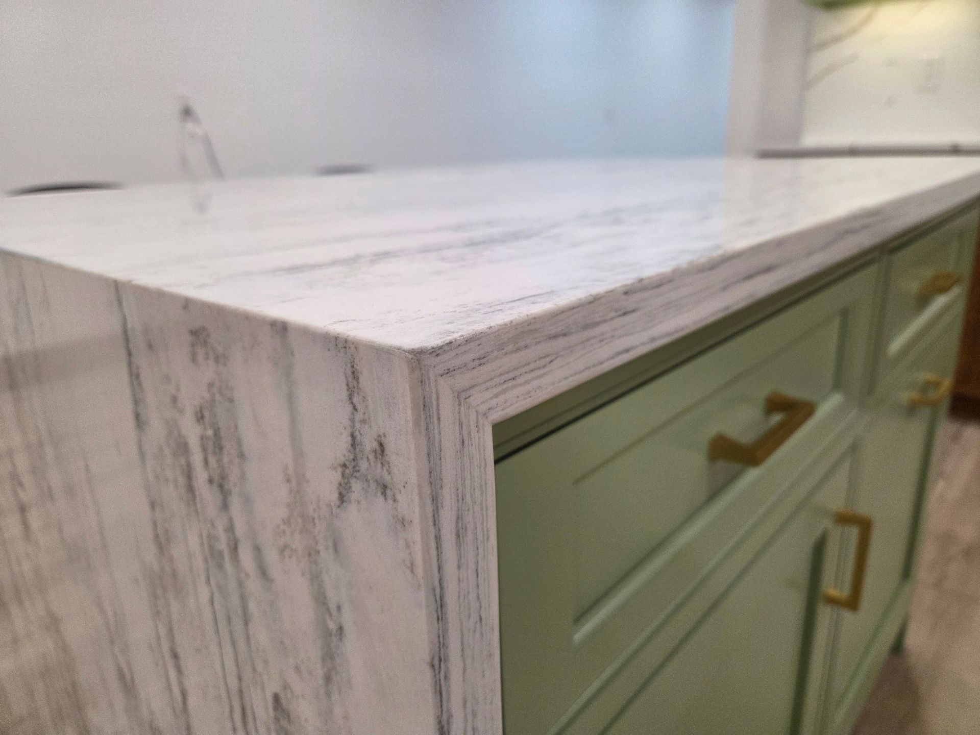 Marble-look countertop edge on a light green kitchen cabinet with brass handles