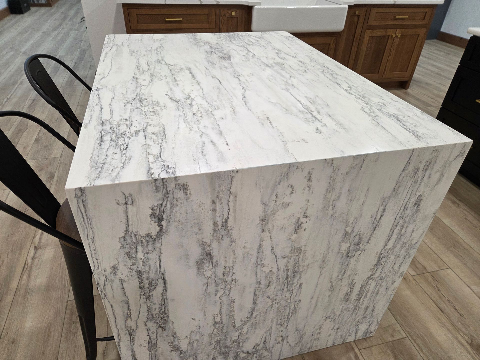 Marble-patterned kitchen island with white top and gray veining, beside black chairs and wood cabinets