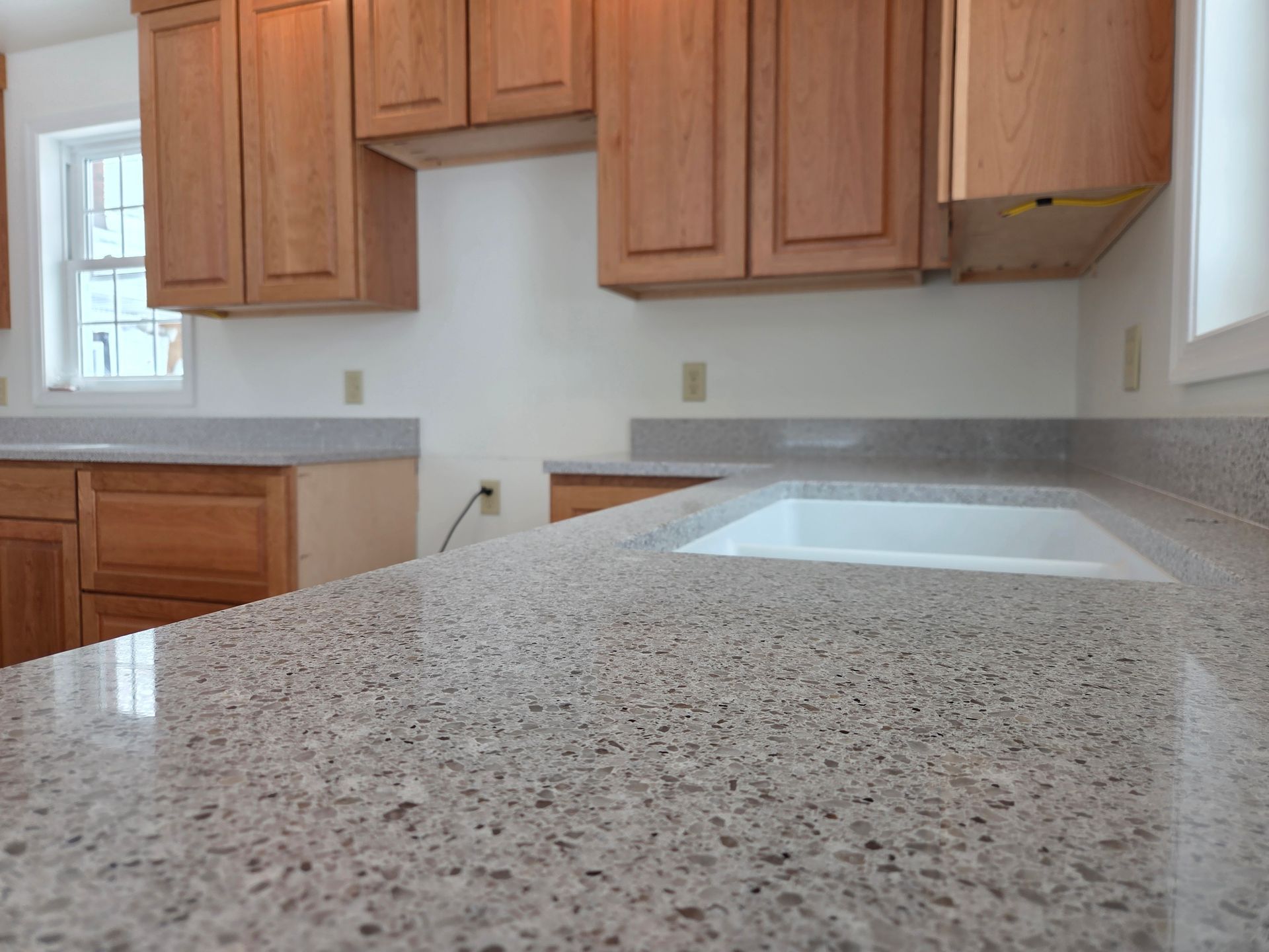 Empty kitchen with speckled granite countertop, wood cabinets, and a window by the sink.