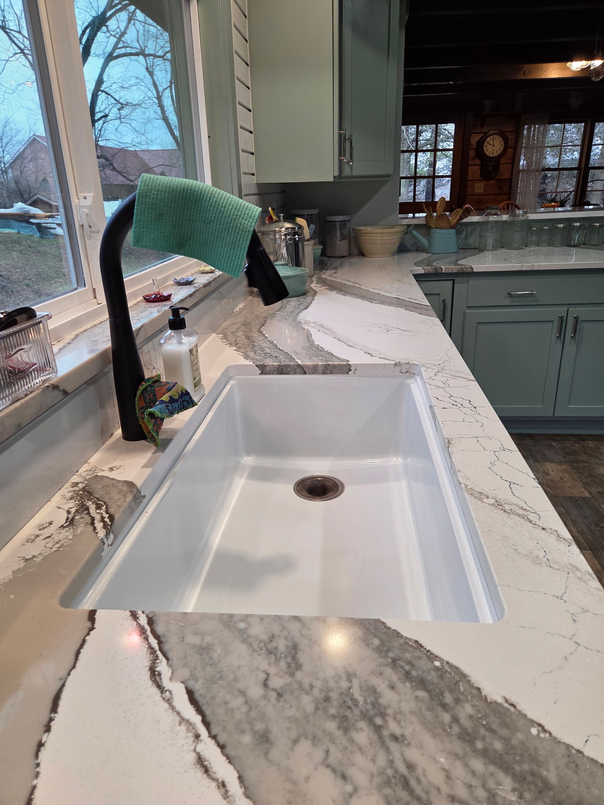 Kitchen sink with white countertop and window, showing a green towel draped over the faucet.