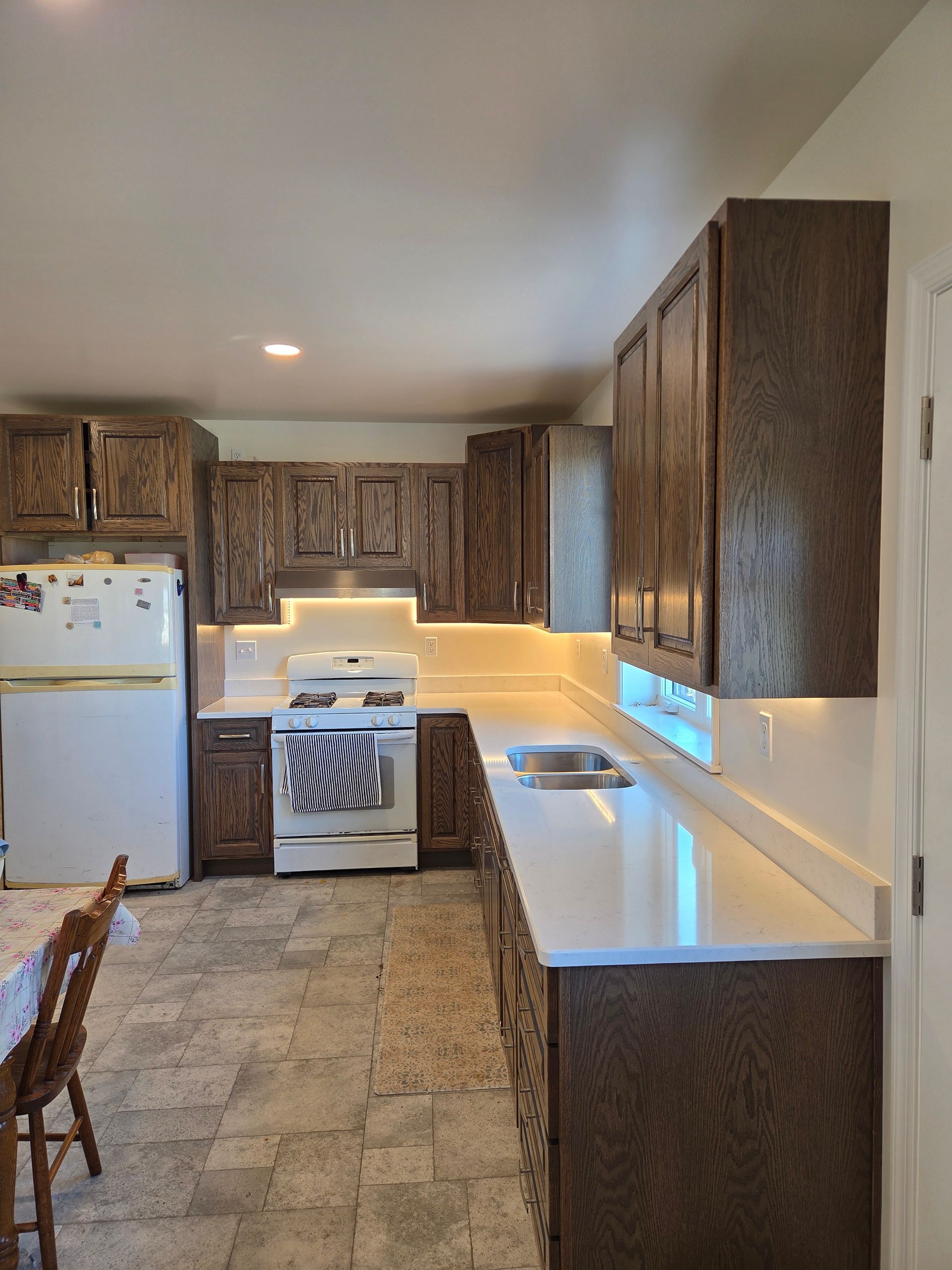 Compact kitchen with wood cabinets, white appliances, and granite countertops under warm under-cabinet lighting