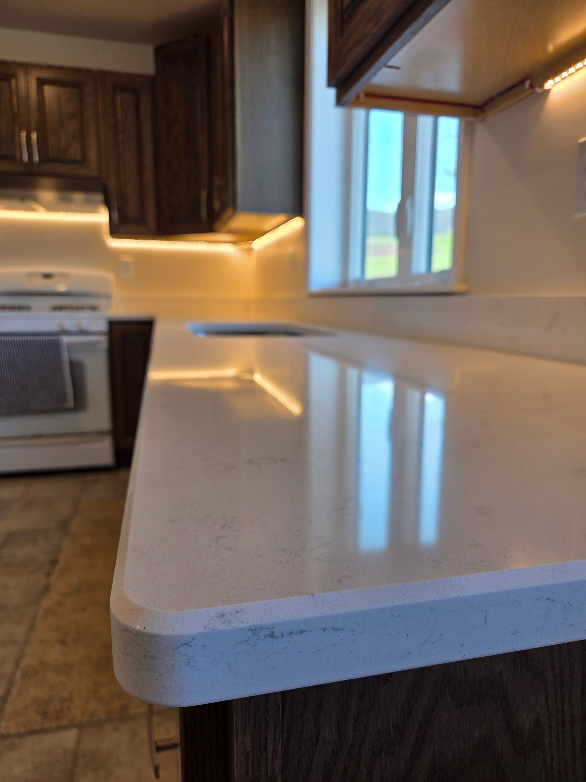 Modern kitchen with white speckled countertop, wood cabinets, stainless stove, and window reflection