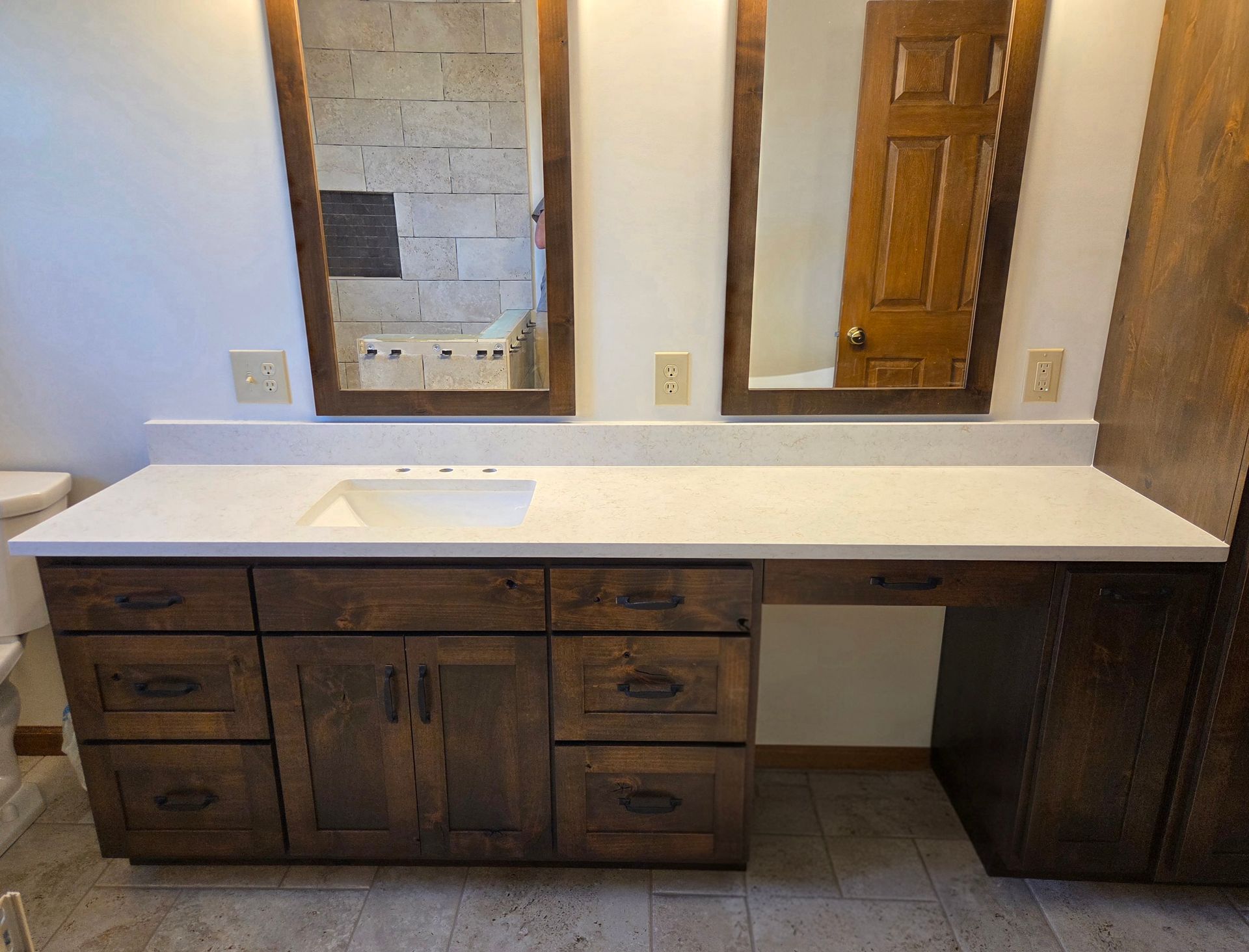 Bathroom vanity with double sinks, dark wood cabinets, white countertop, and wall mirror