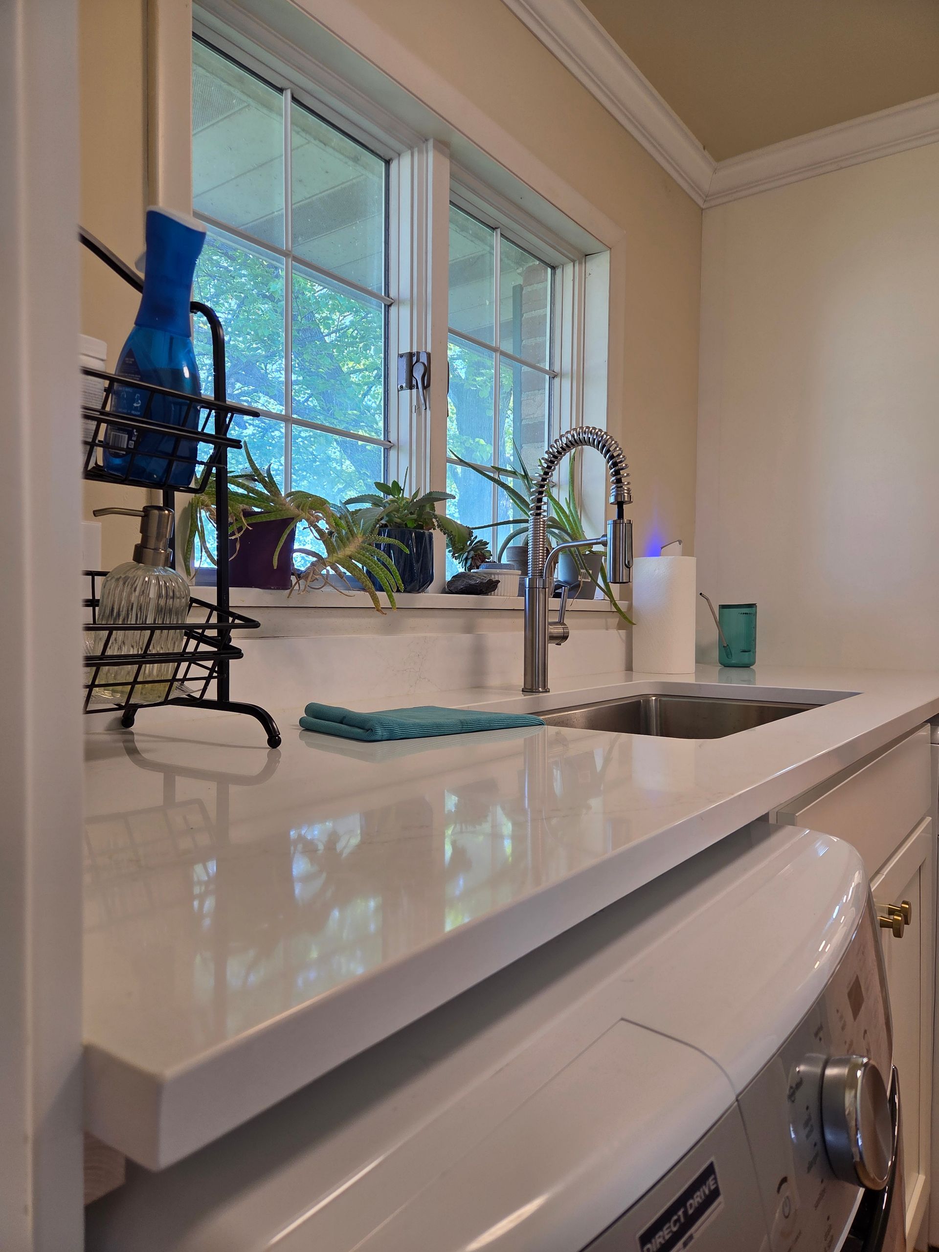 Bright bathroom vanity with white countertop, chrome faucet, window, potted plant, and blue vase.