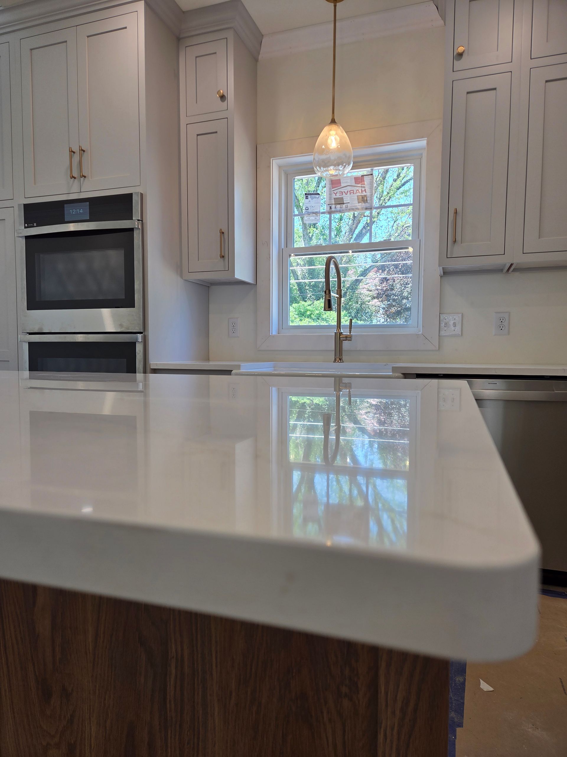 Bright modern kitchen with white cabinets, built-in oven, pendant light, and a glossy island reflecting a window.