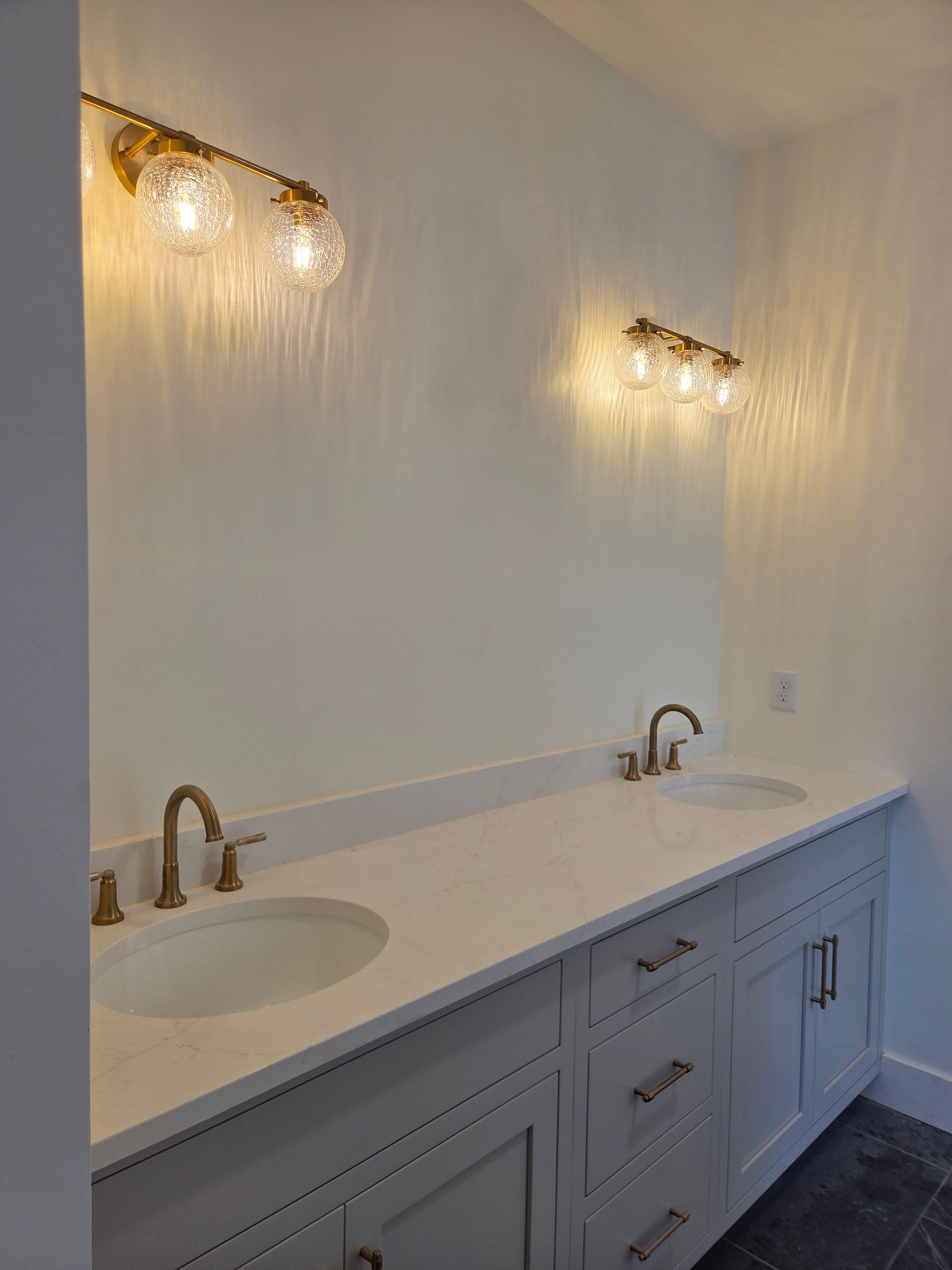 Modern double vanity with white countertop, brass faucets, and lit wall sconces in a bathroom