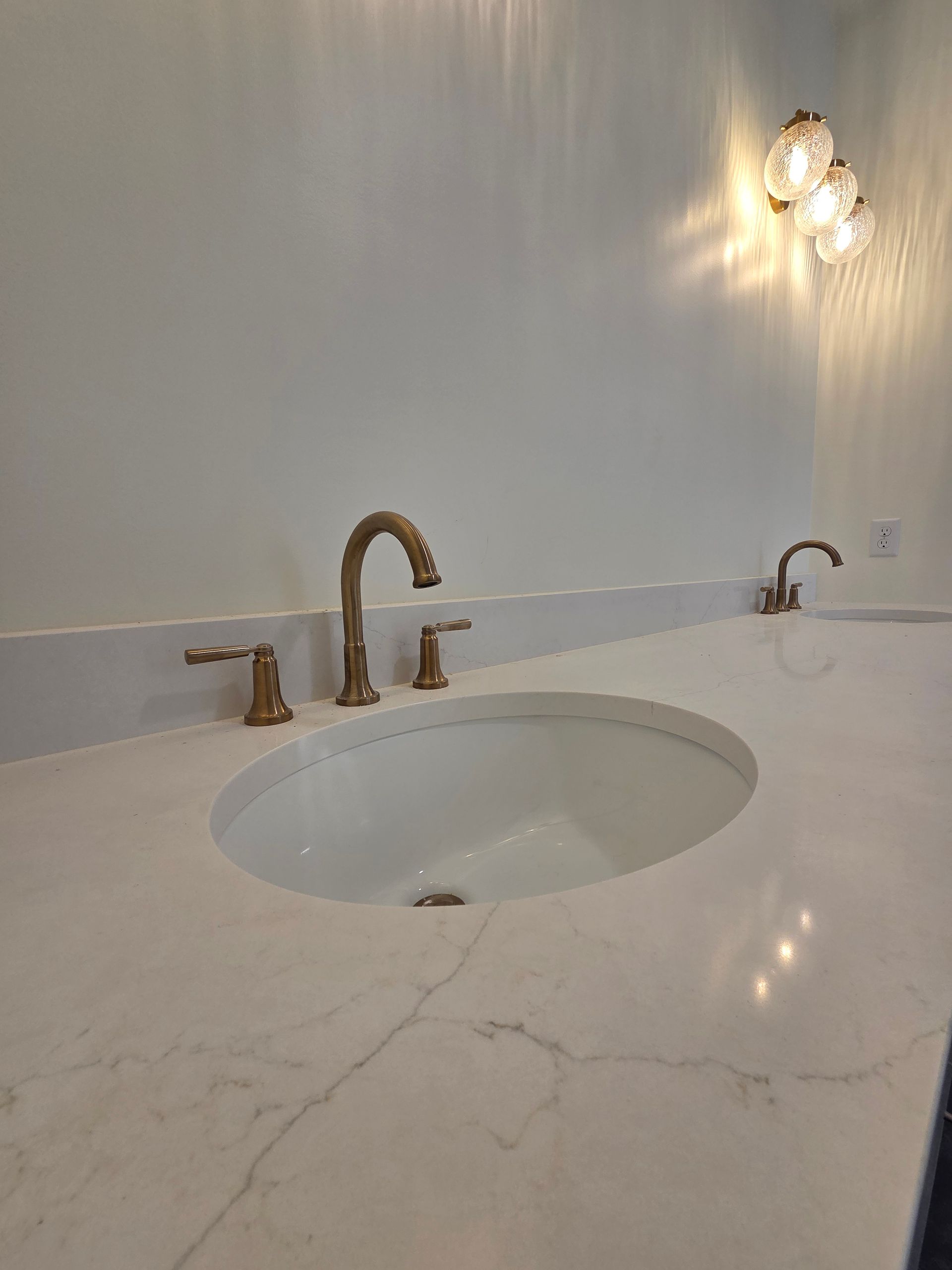 Modern white bathroom vanity with marble countertop, oval sink, and gold faucet under wall sconces