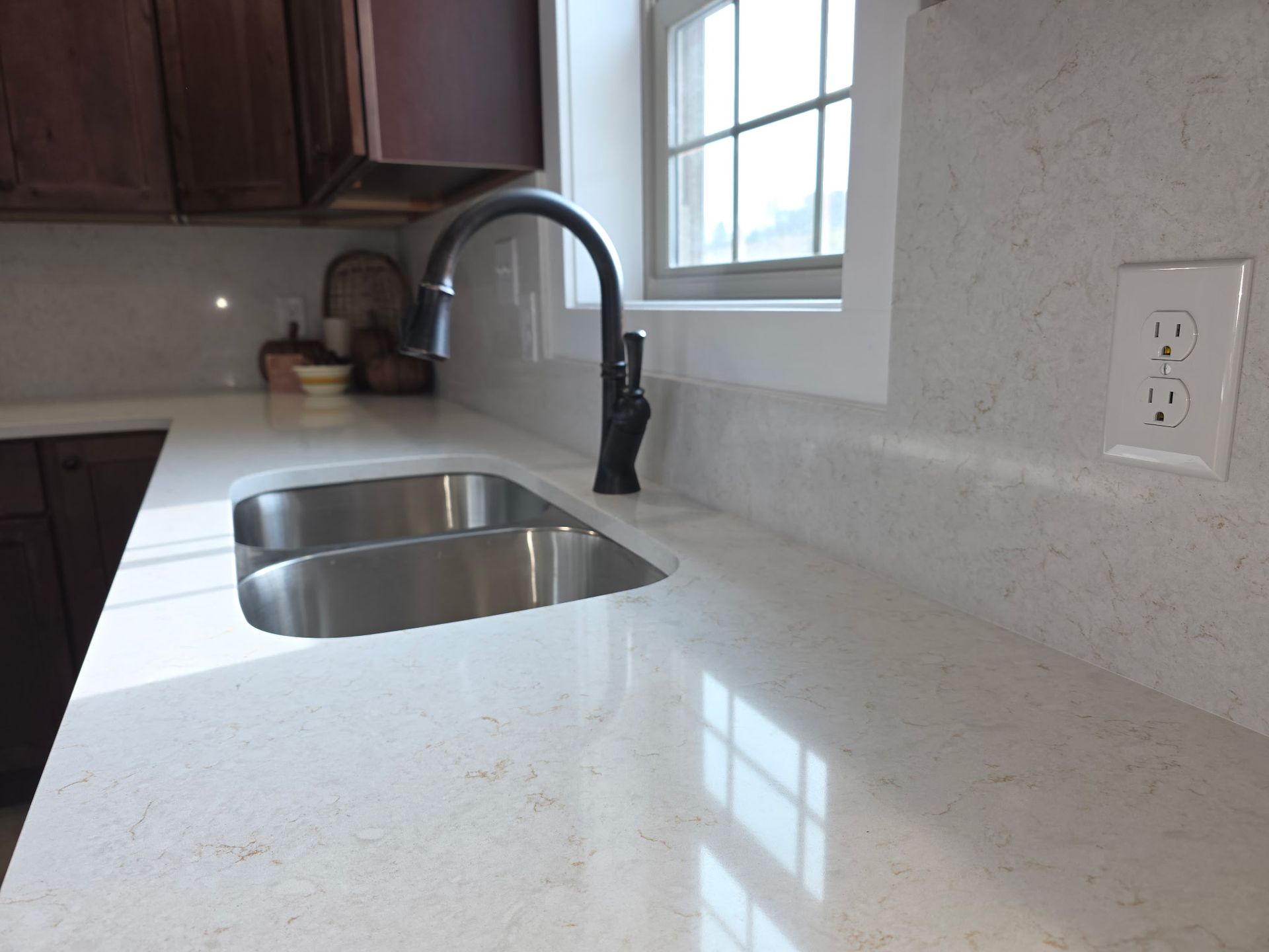 Modern kitchen countertop with stainless sink, black faucet, and window reflection