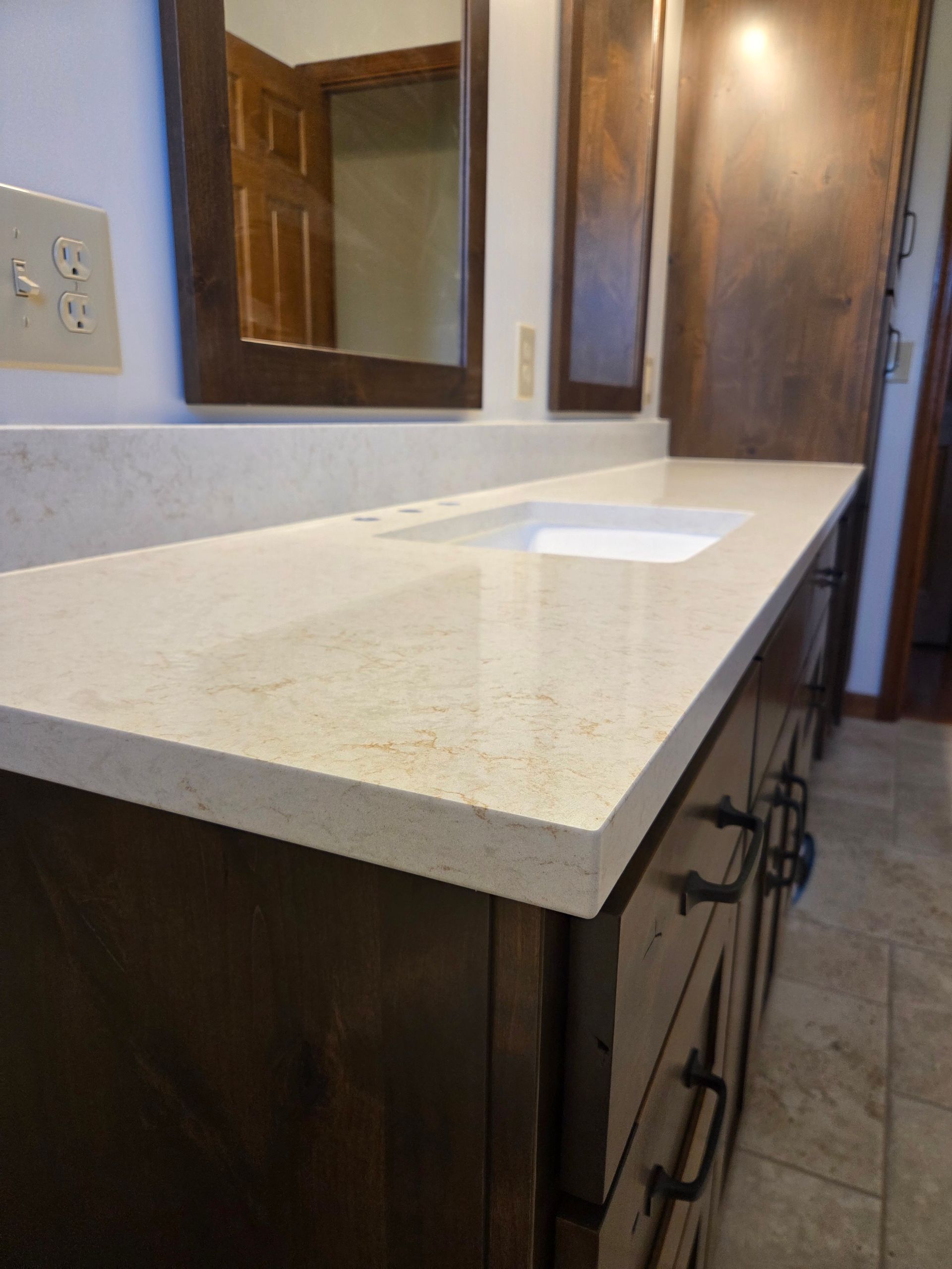 Bathroom vanity with speckled countertop, built-in sink, and wall mirror above dark wood cabinets.