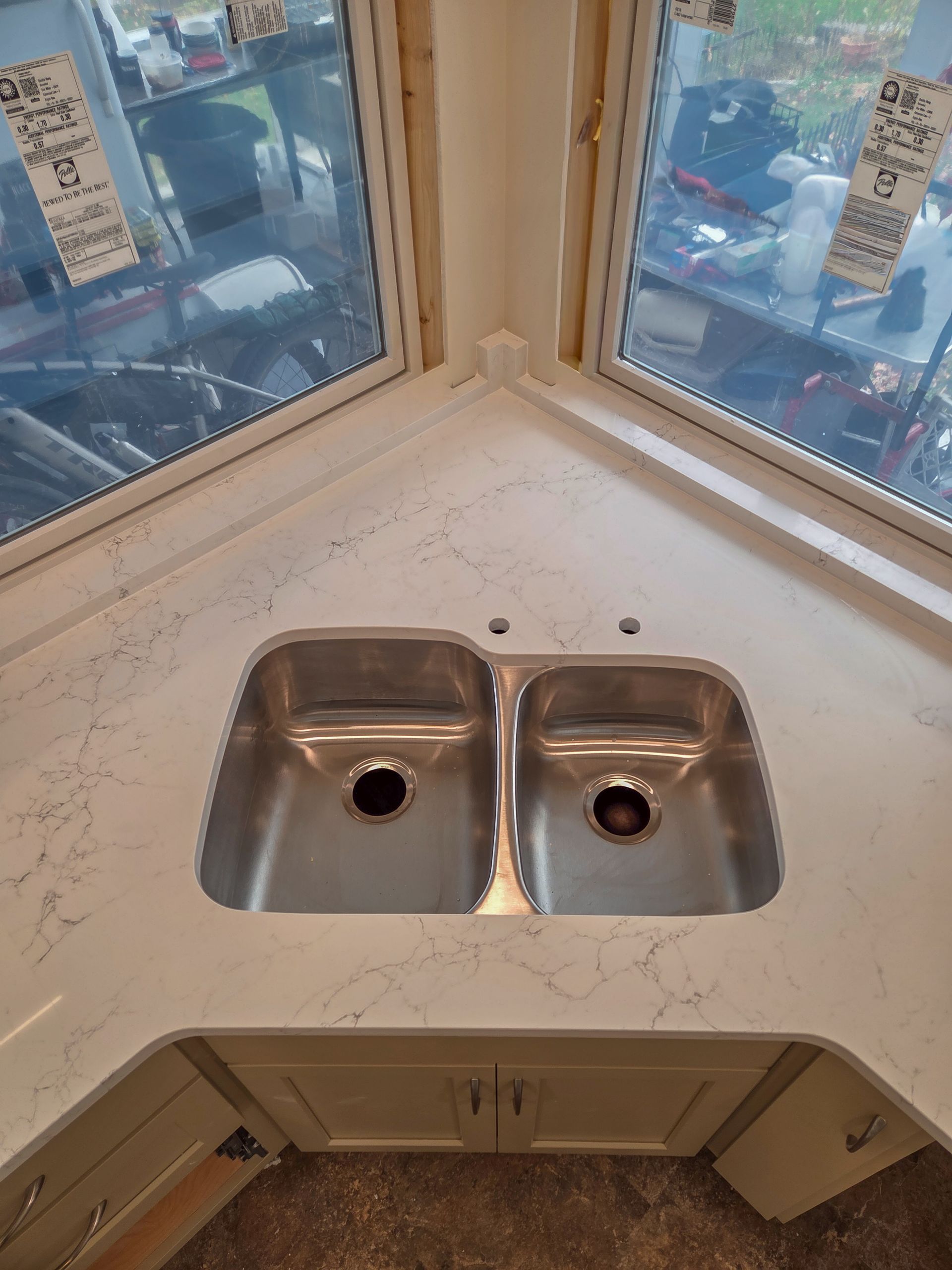Corner kitchen sink with two stainless steel basins and white countertop by windows