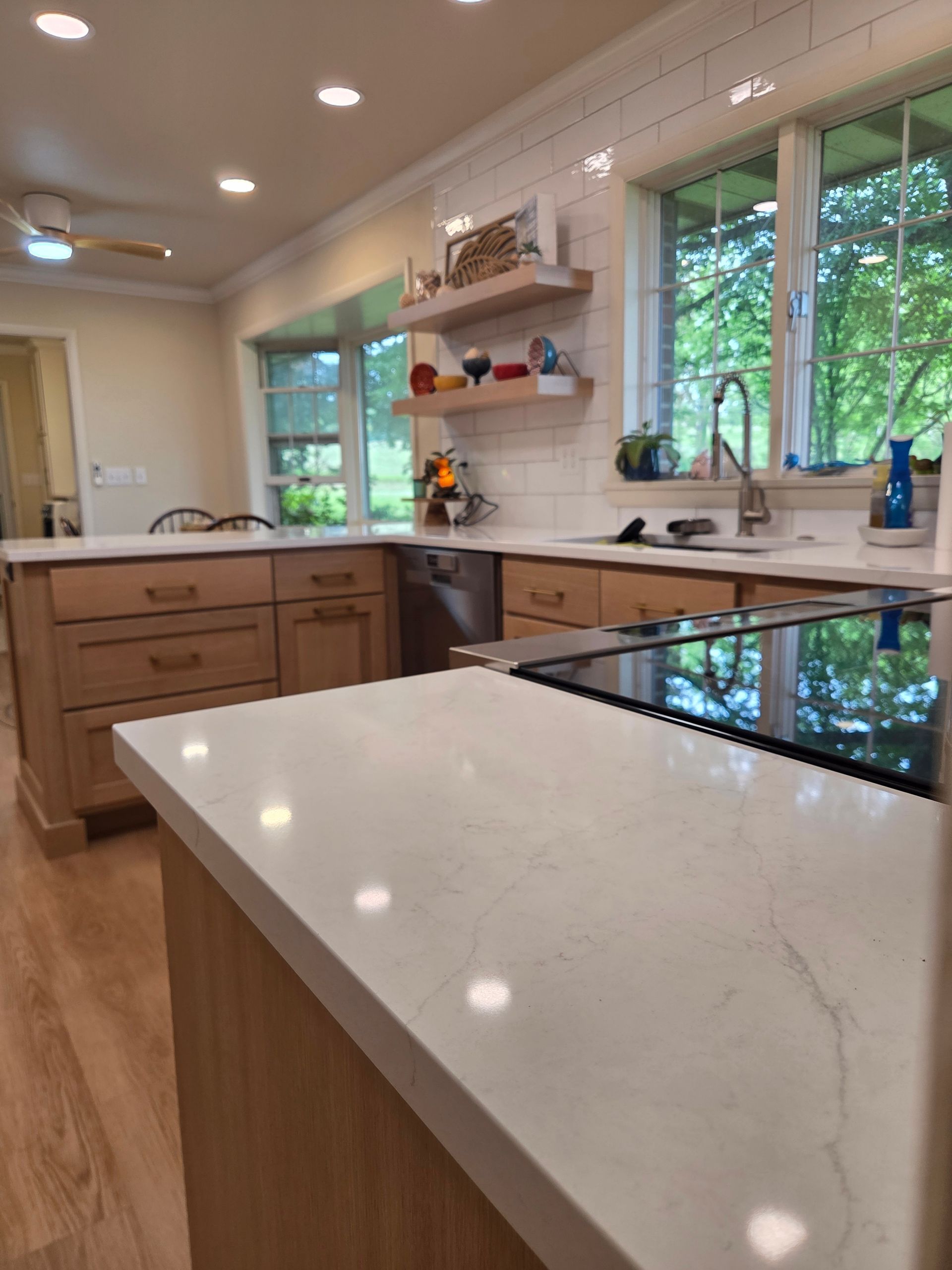 Modern kitchen with white island, wood cabinets, and large windows overlooking greenery
