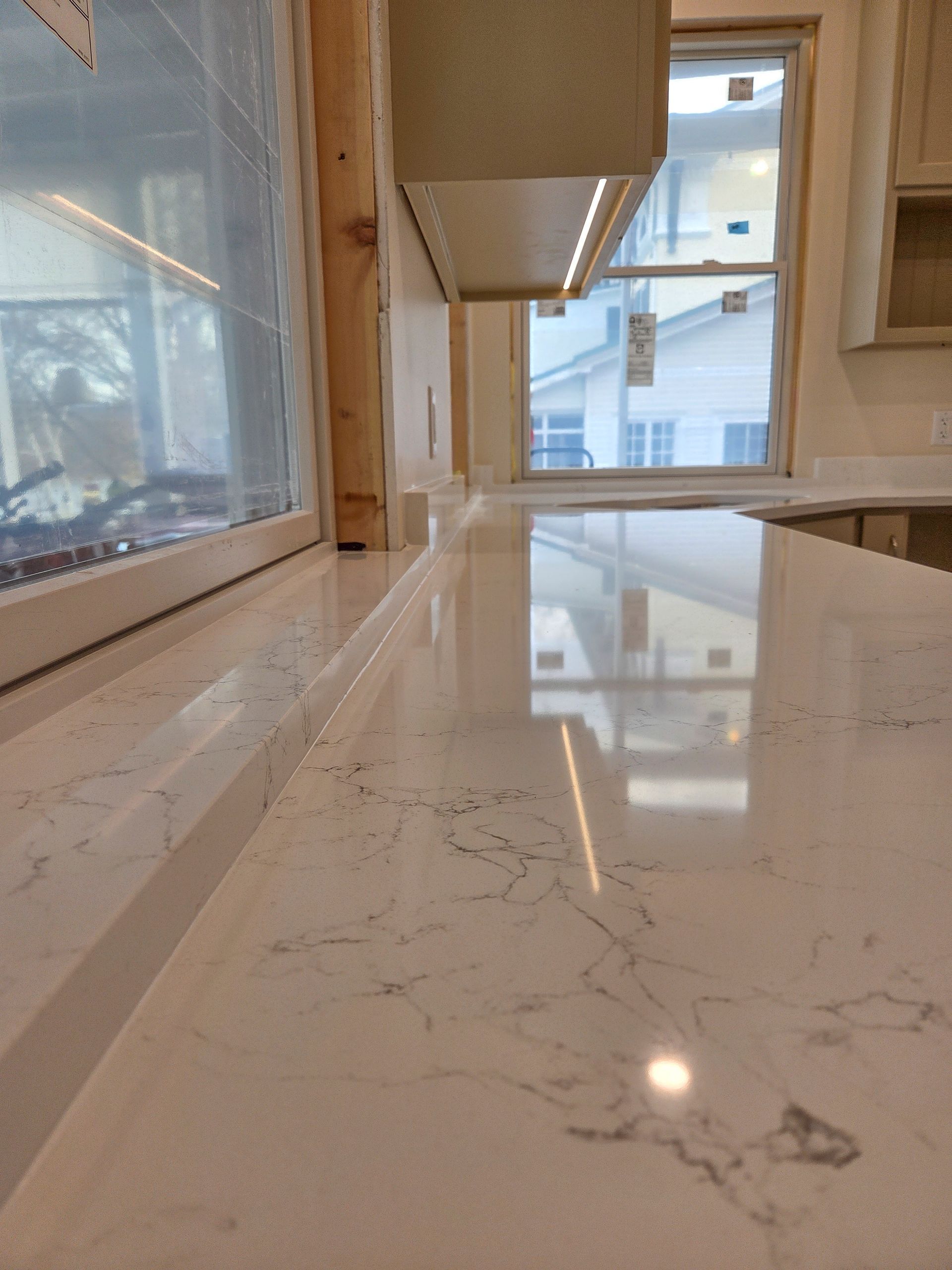 Bright marble kitchen countertop by a window, reflecting the room and a hanging vent hood.