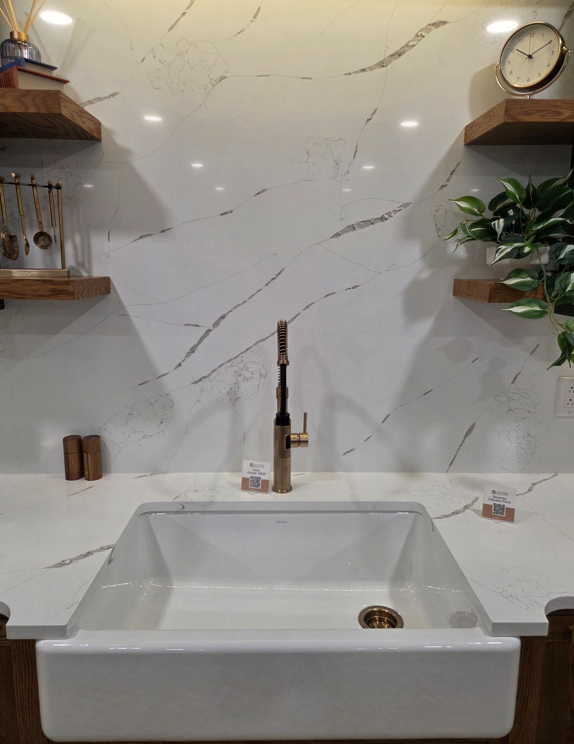 Modern bathroom vanity with white stone sink, gold faucet, marble wall, shelf, clock, and plant