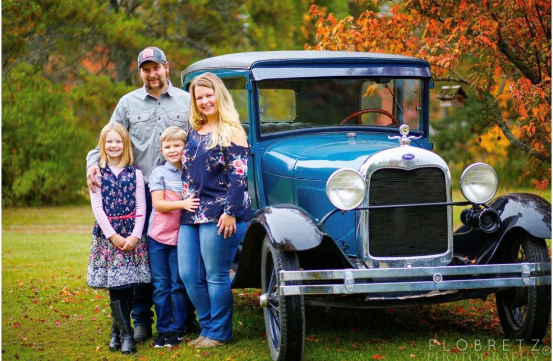 a family is posing for a picture in front of an old truck .