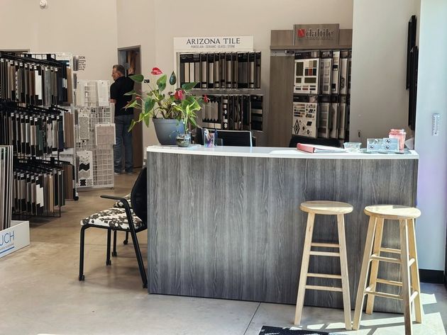 Retail store counter with gray wood front, two stools, and floor tile samples