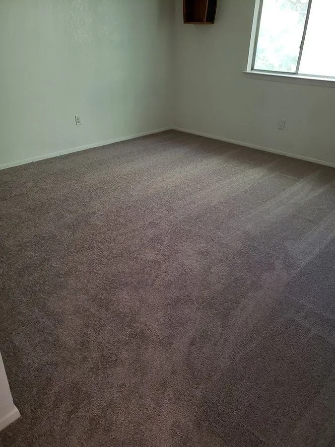Empty beige carpeted room with white walls and a window on the right.