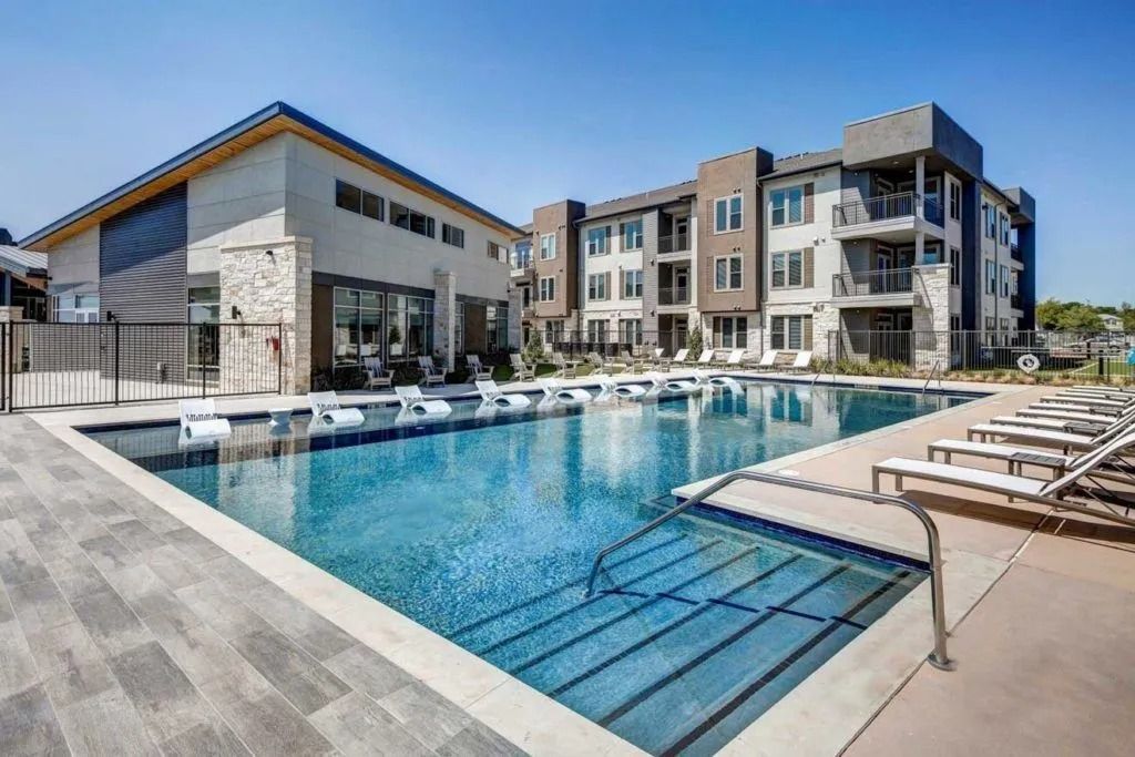 Modern apartment complex with outdoor swimming pool and lounge chairs under a clear blue sky