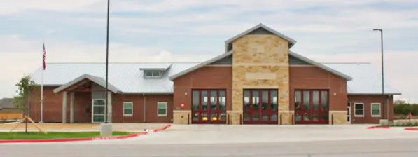 Brick school building with central stone entrance and red doors under a clear sky