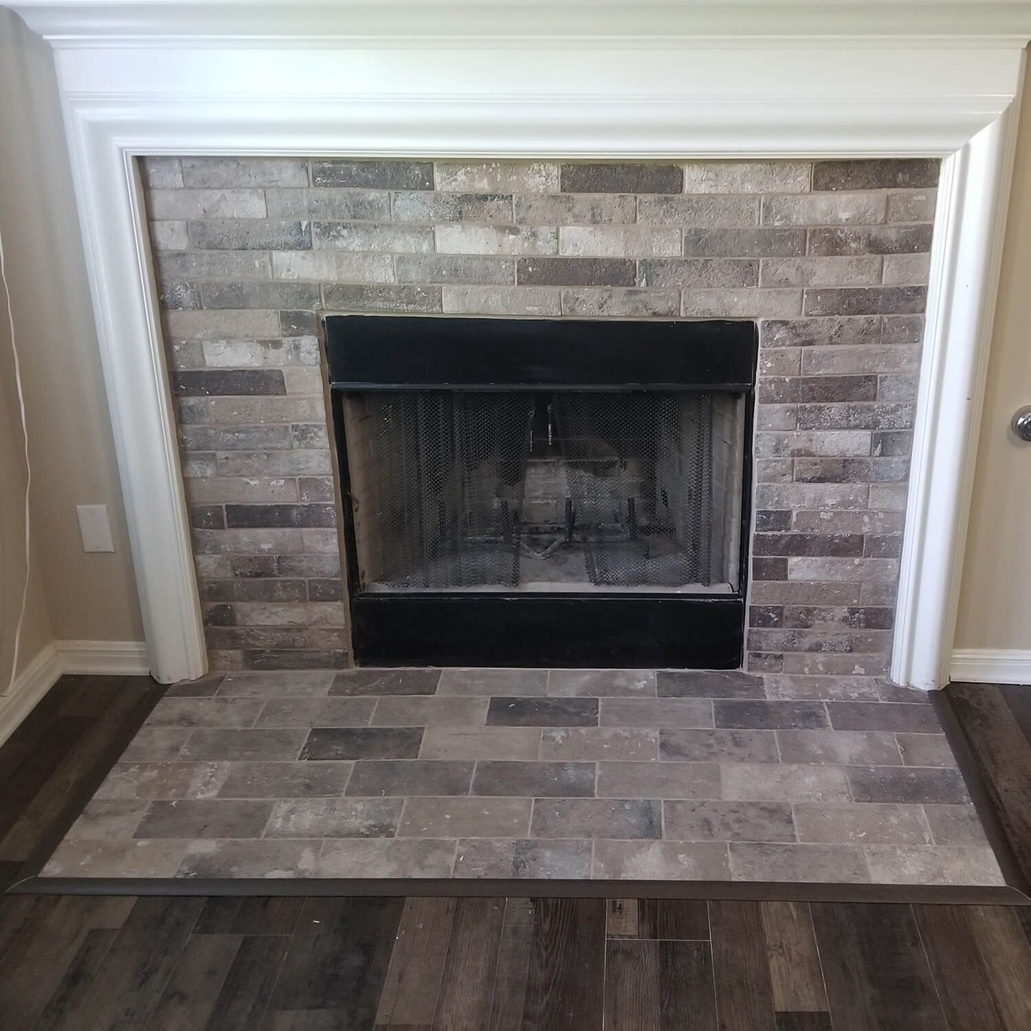 Stone fireplace with black firebox and white mantel in a room with dark wood flooring