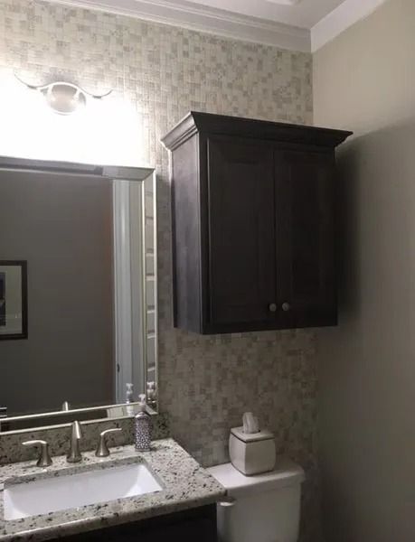 Small bathroom with dark wall cabinet, mirror, sink, and toilet under a light fixture.