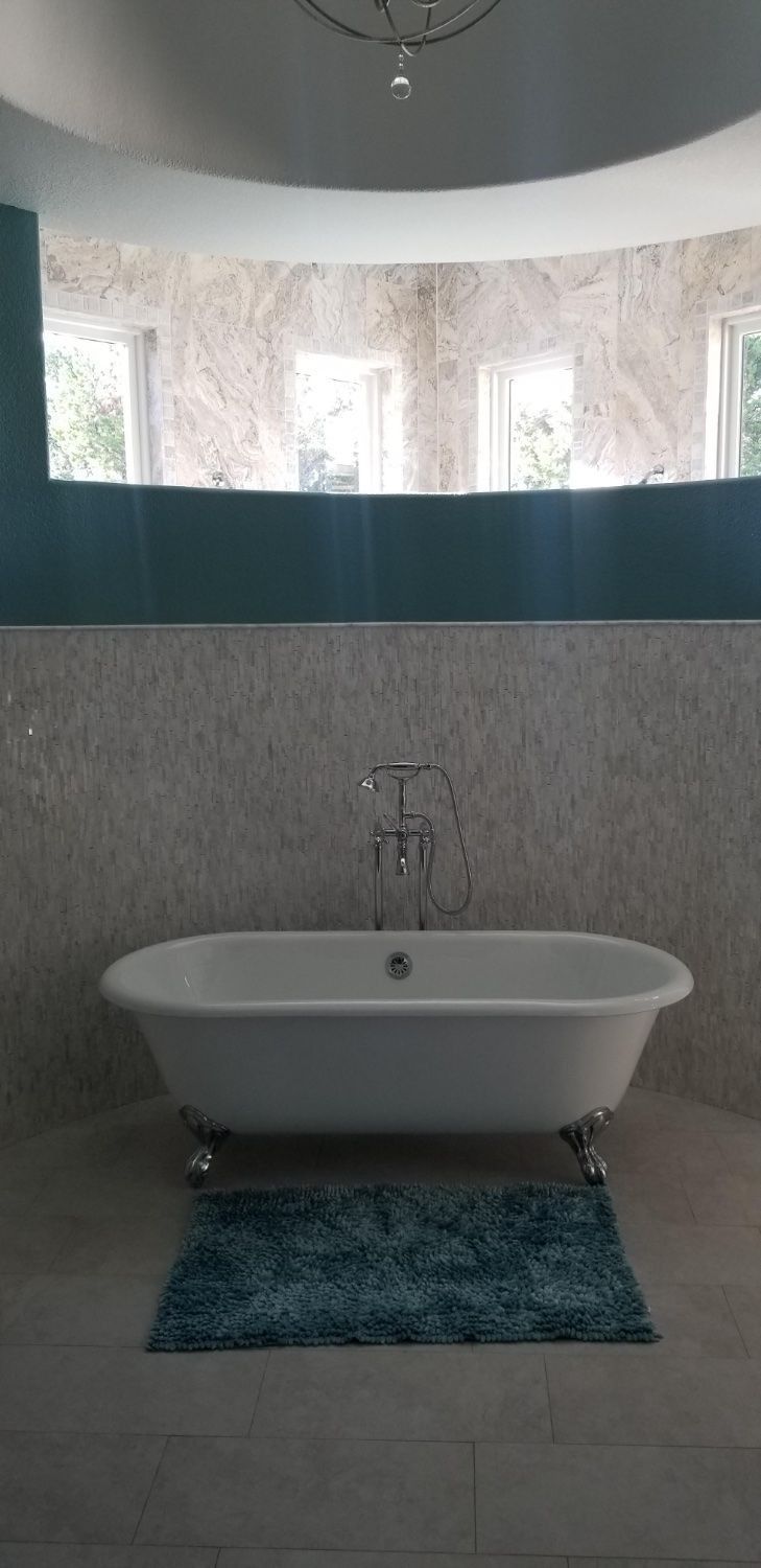 Modern bathroom with a white bathtub, blue rug, and tiled walls under a windowed partition
