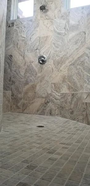 Stone-tiled public shower with a central wall-mounted showerhead and tiled floor.