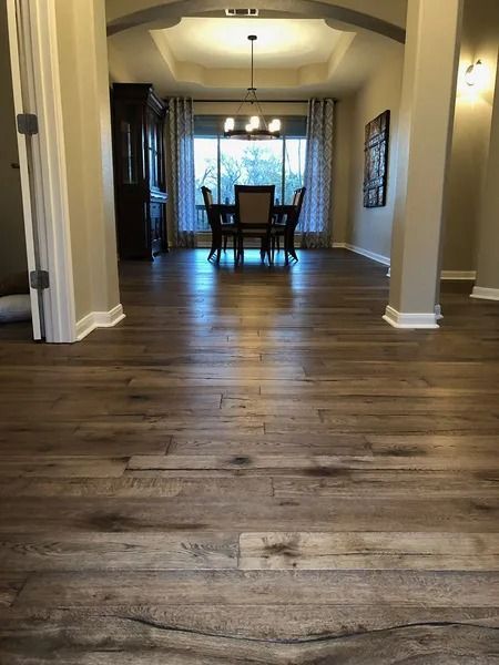 Hallway with dark wood floors leading to a dining room and chandelier under soft natural light