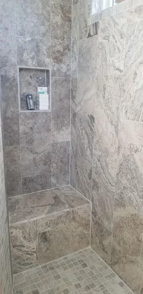 Stone-tiled walk-in shower with built-in bench and recessed shelf, empty and clean.
