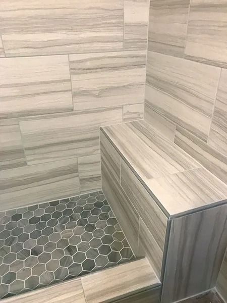 Tiled shower with gray hex floor, beige wall tiles, and built-in bench seat