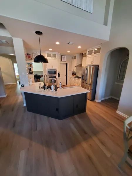 Bright modern kitchen with a large island, stainless fridge, pendant lights, and warm wood floors