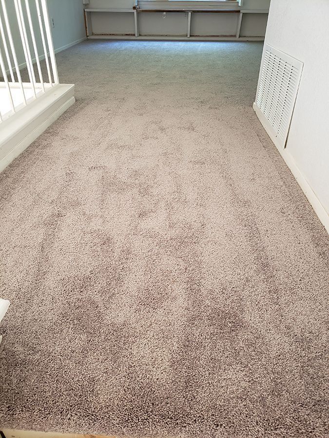 Empty beige carpeted hallway with white walls and a vent on the right side