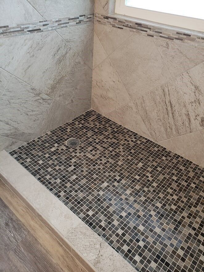 Corner shower with beige stone walls and a dark mosaic tile floor