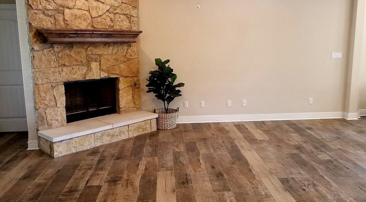 Empty living room with stone fireplace, wood-look flooring, and beige walls