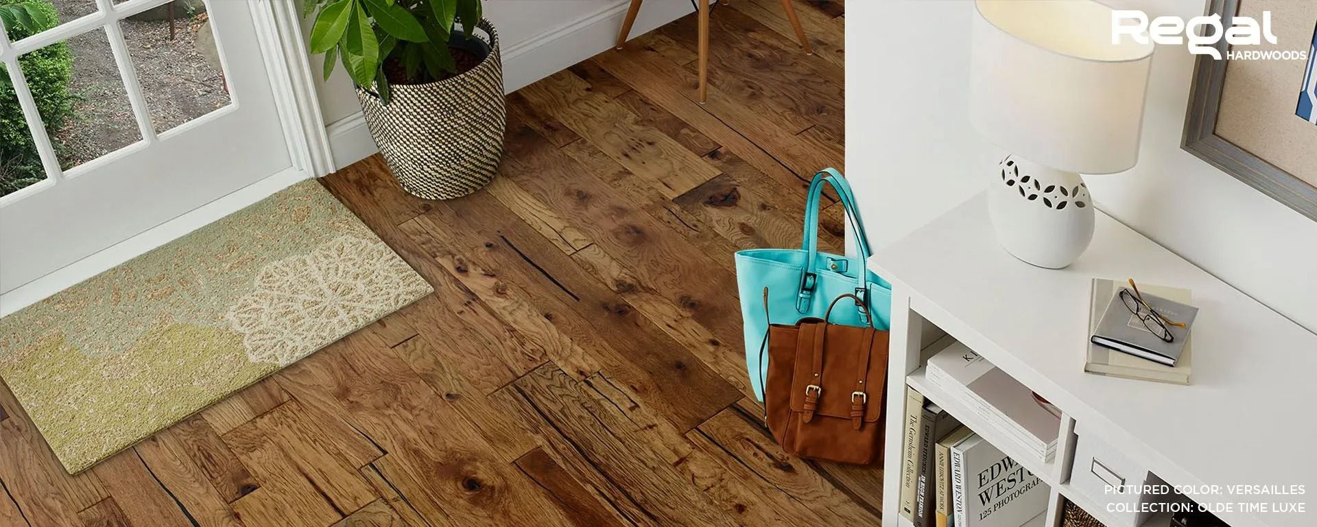 Entryway with wood floor, green rug, potted plant, and turquoise tote by a white console table.