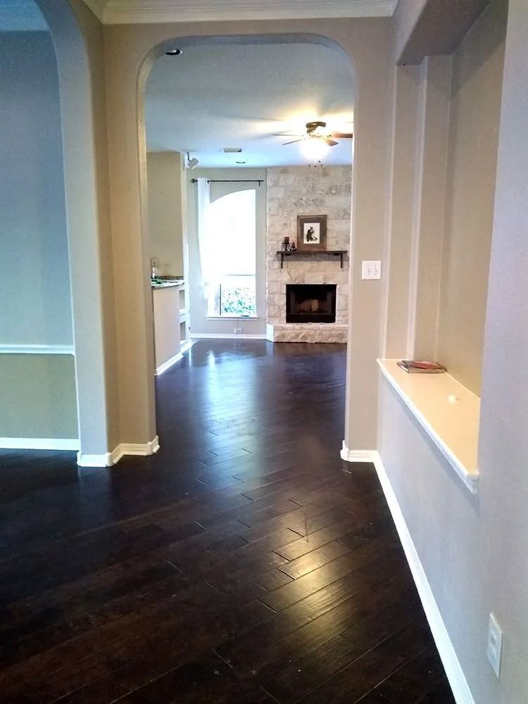 Empty hallway with dark wood floors leading to a living room and fireplace.