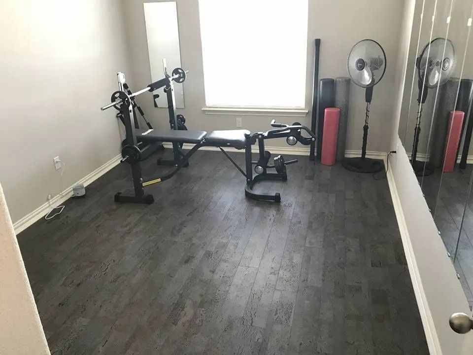 Empty home gym with bench, weight machine, mirrors, and two fans by a window